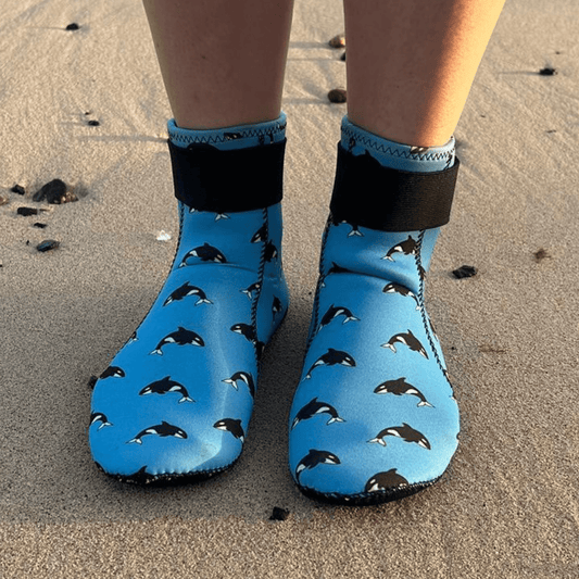 Blue neoprenebeach shoes with orca pattern worn on sandy ground