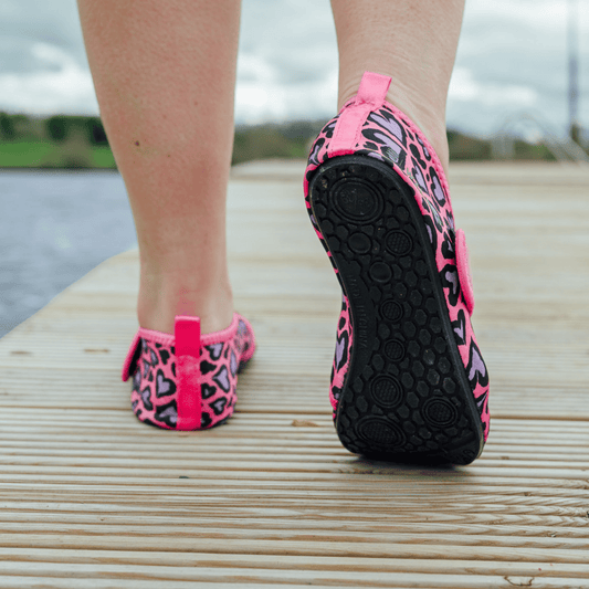 Pink and black patterned neoprene beach shoes on a wooden deck with a blurred natural background