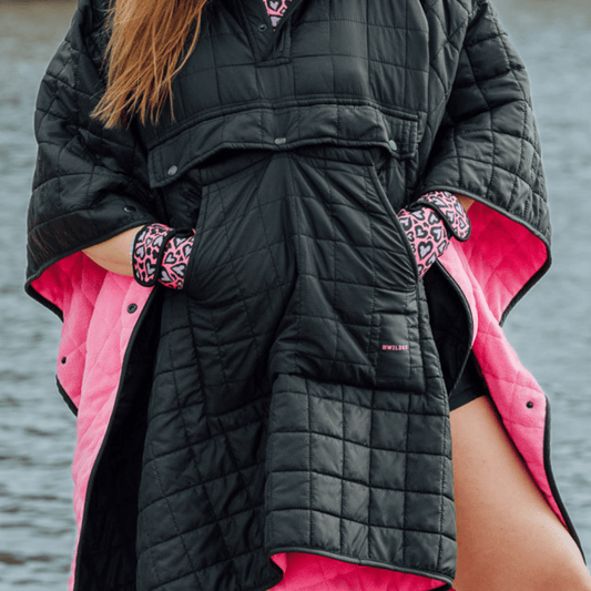 Image of woman wearing weatherproof black robe with large front pocket, side popper fastening, hood and pink fleece lining