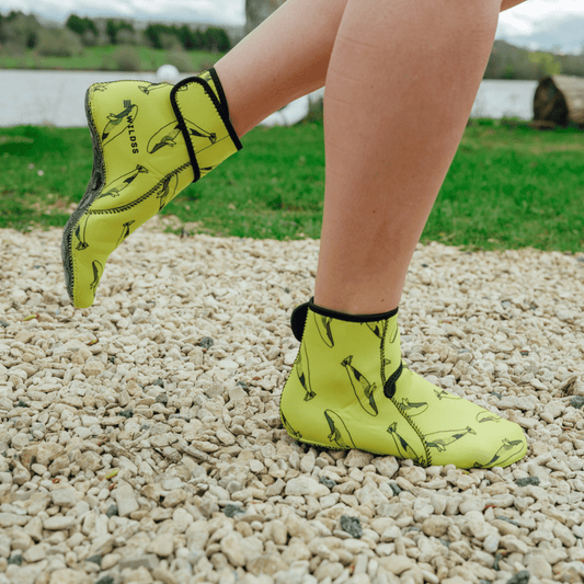 Person wearing bright yellow neoprene booties with black patterns on a gravel surface.