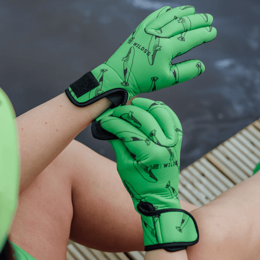 Green neoprene gloves with whale designs on a person's hands against a blurred natural background