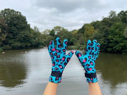Person wearing turquoise leopard print neoprene swimming gloves, hands raised by a lake