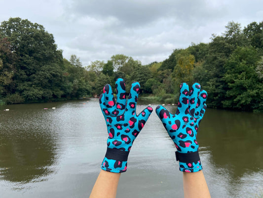Person wearing turquoise leopard print neoprene swimming gloves, hands raised by a lake
