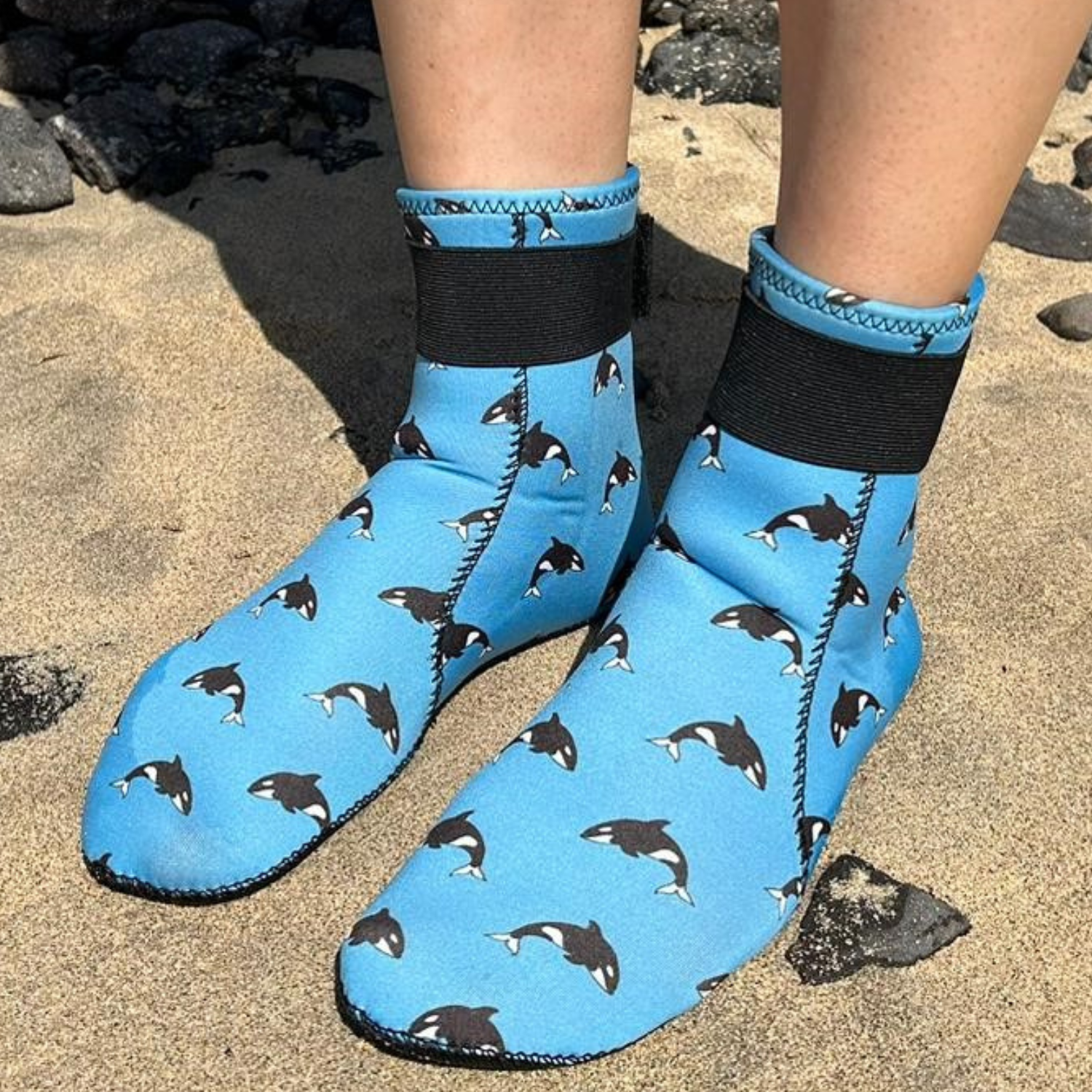 Blue neoprene socks with black and white patterns worn on a sandy surface