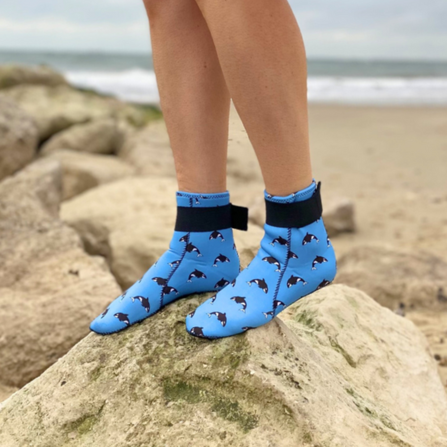 Person wearing blue neoprene socks with dog pattern on a rocky beach