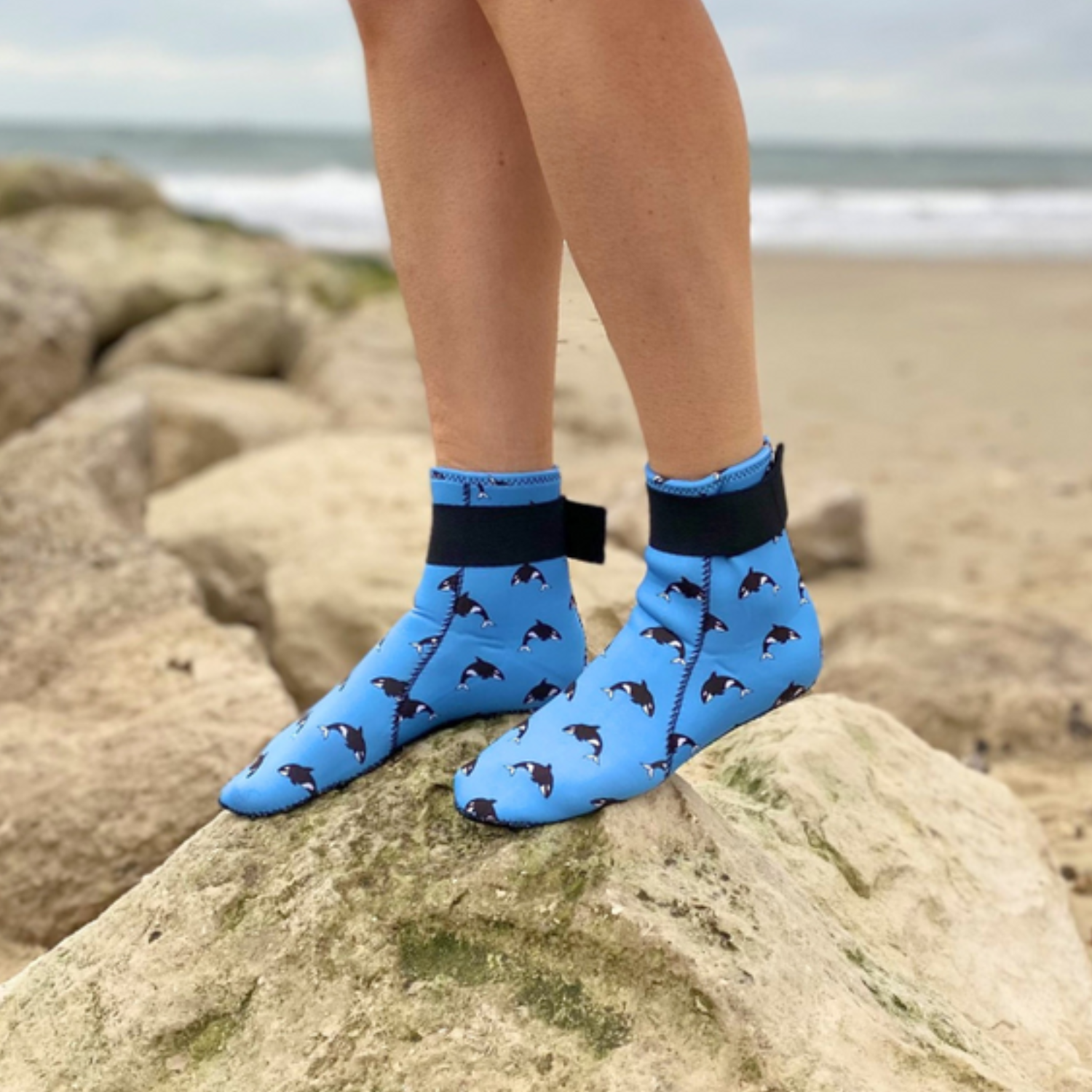 Person wearing blue neoprene socks with dog pattern on a rocky beach