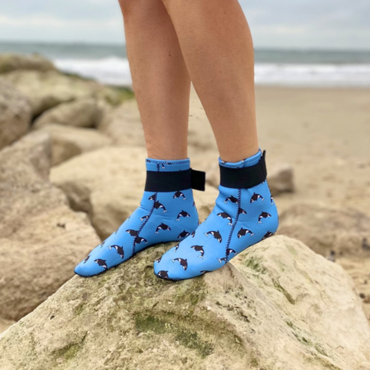 Person wearing blue neoprene socks with dog pattern on a rocky beach