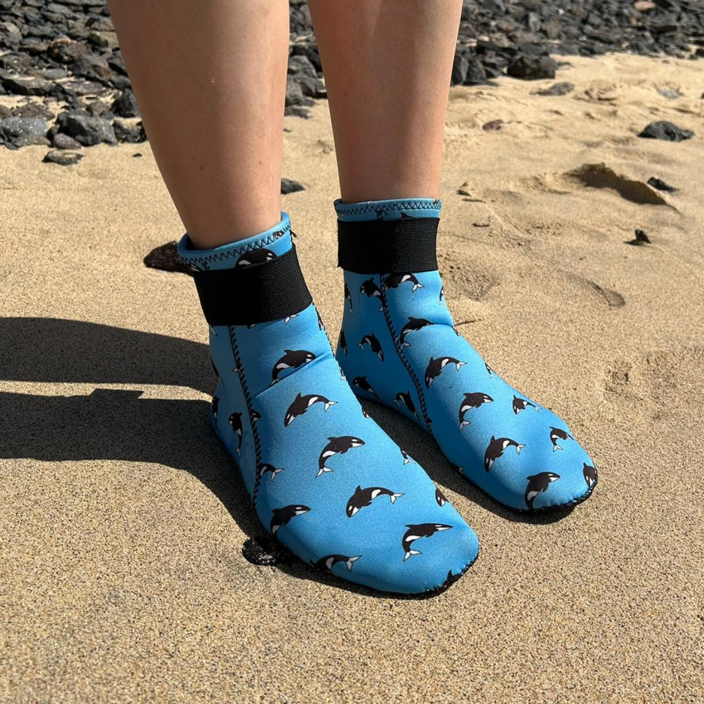 Blue neoprene beach shoes with shark pattern worn on a sandy surface