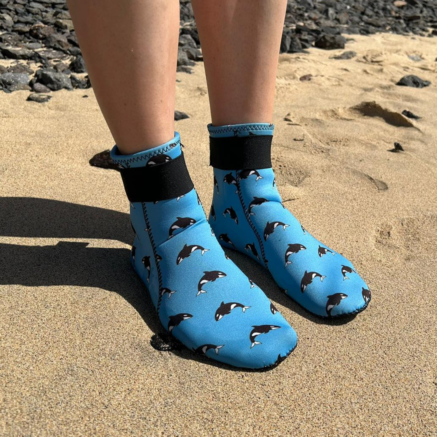 Blue neoprene beach shoes with shark pattern worn on a sandy surface