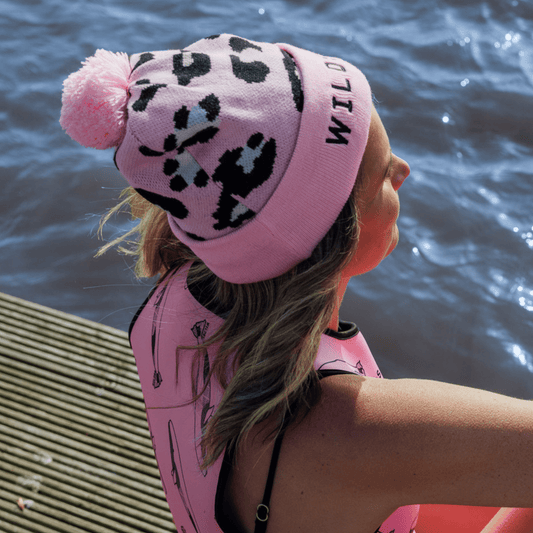 Person wearing a bright pink leopard print beanie hat and matching pink neoprene swimming gear.
