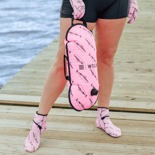 Person wearing tow float and neoprene swimming gear by water.