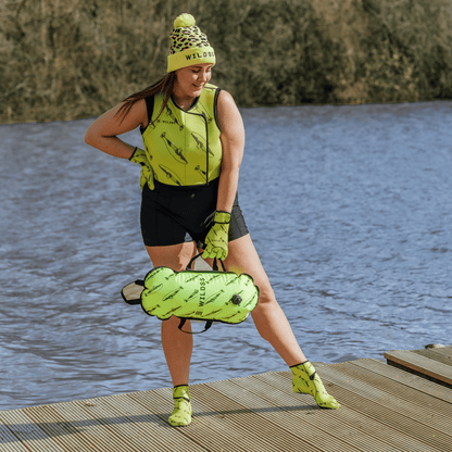 Person wearing yellow leopard print hat and neoprene swimming gear by water.