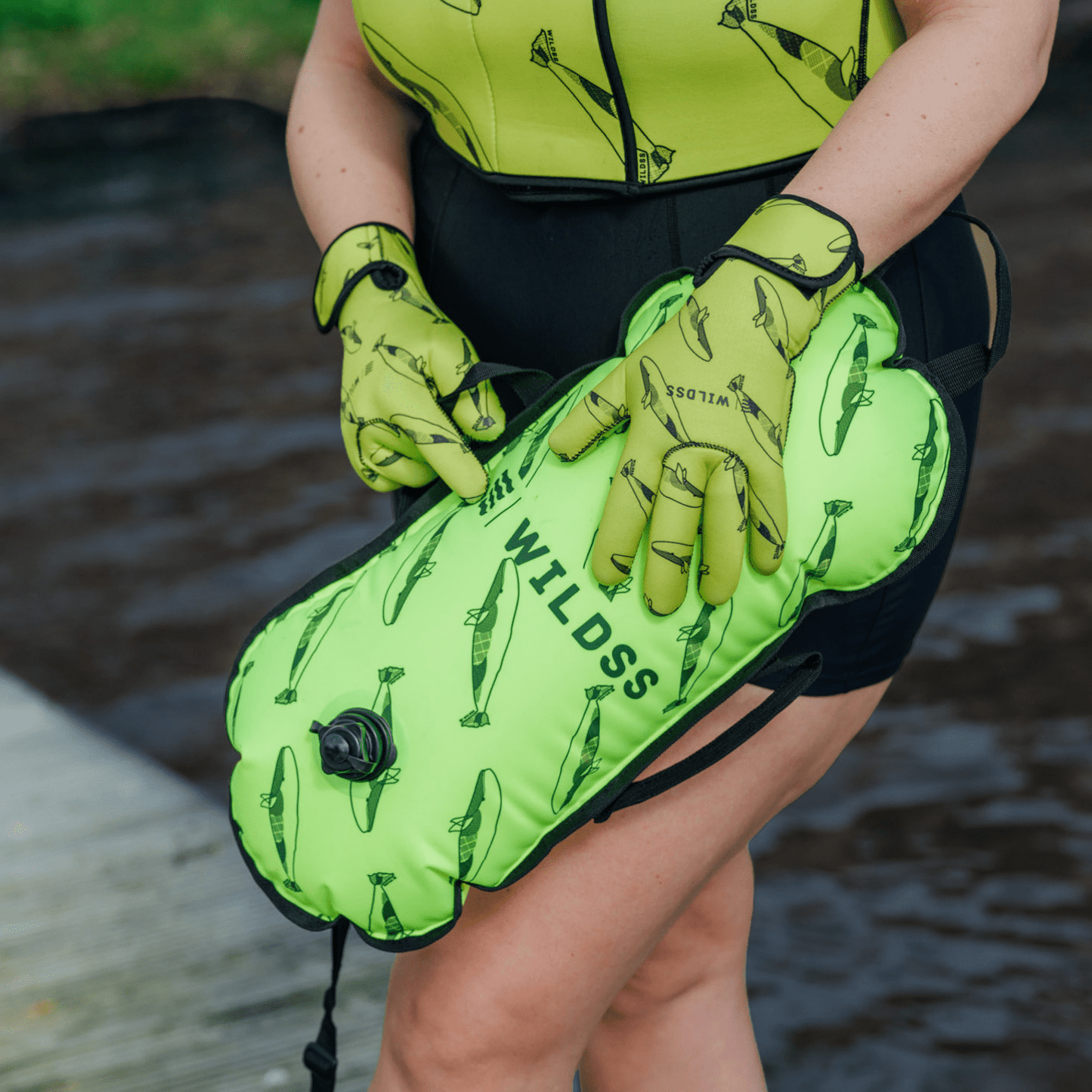 Person wearing yellow tow float and neoprene swimming gear by water.