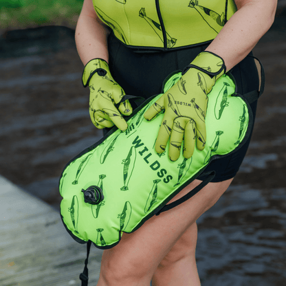 Person wearing yellow tow float and neoprene swimming gear by water.