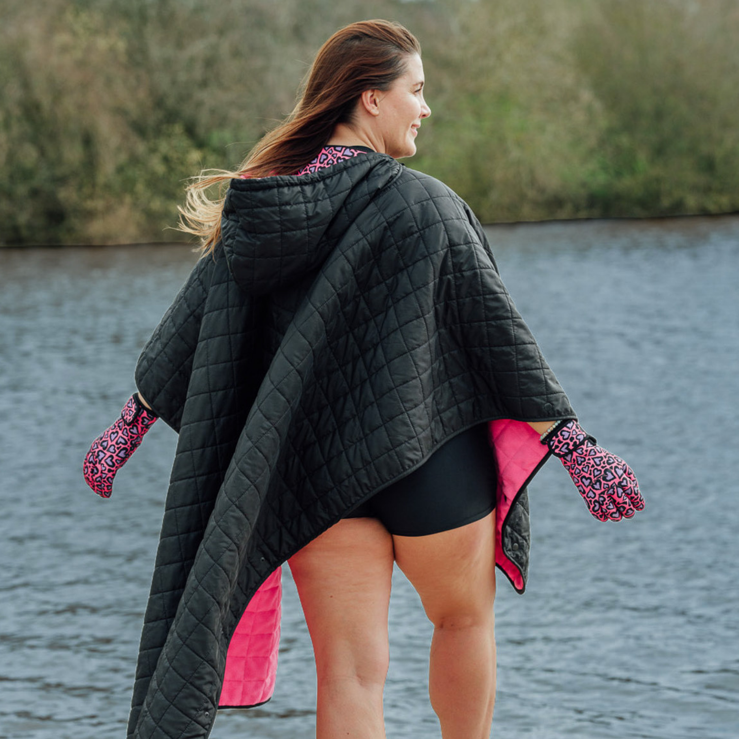 Image of woman wearing weatherproof black robe with large front pocket, side popper fastening, hood and pink fleece lining