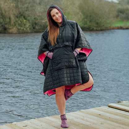 Image of woman wearing weatherproof black robe with large front pocket, side popper fastening, hood and pink fleece lining