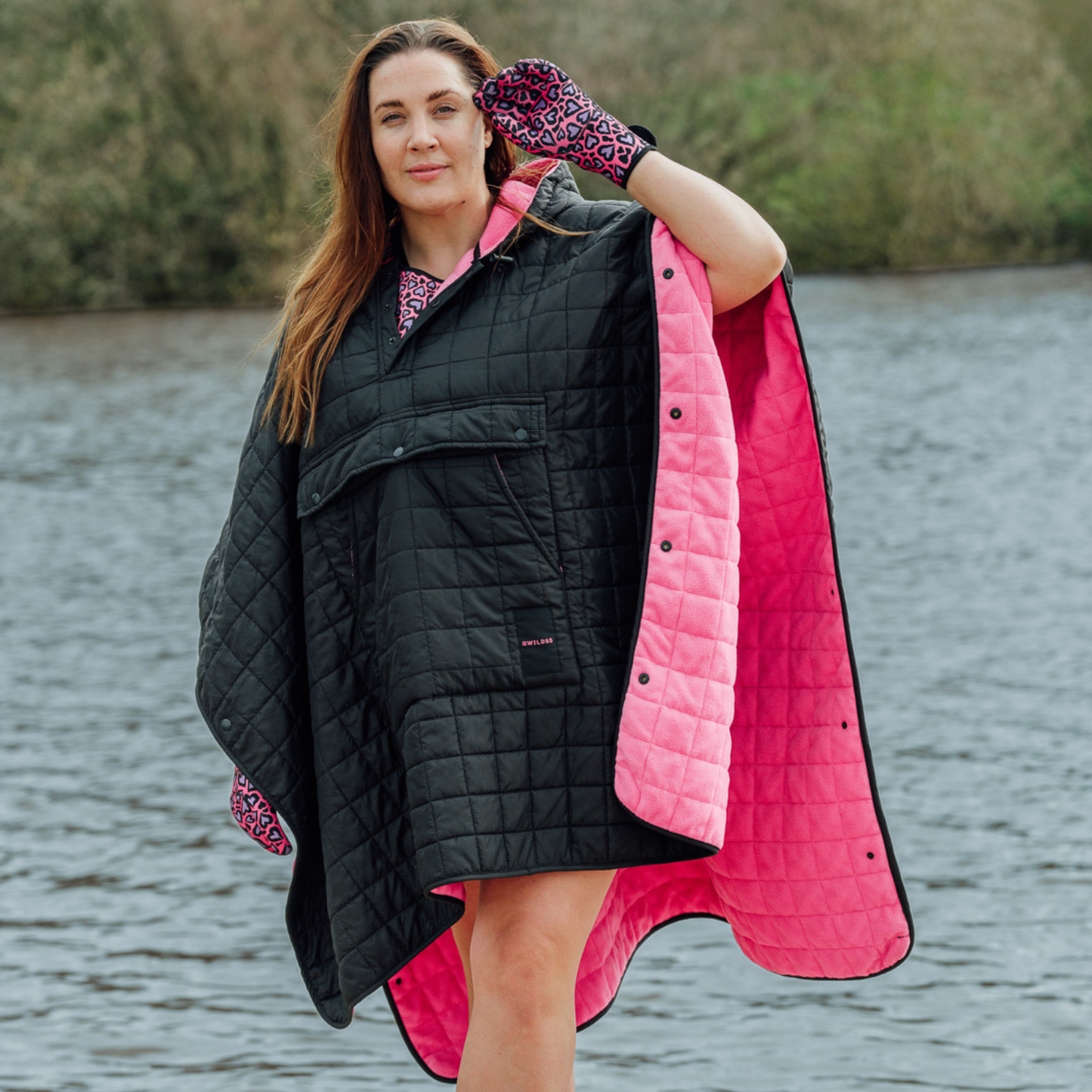 Image of woman wearing weatherproof black robe with large front pocket, side popper fastening, hood and pink fleece lining