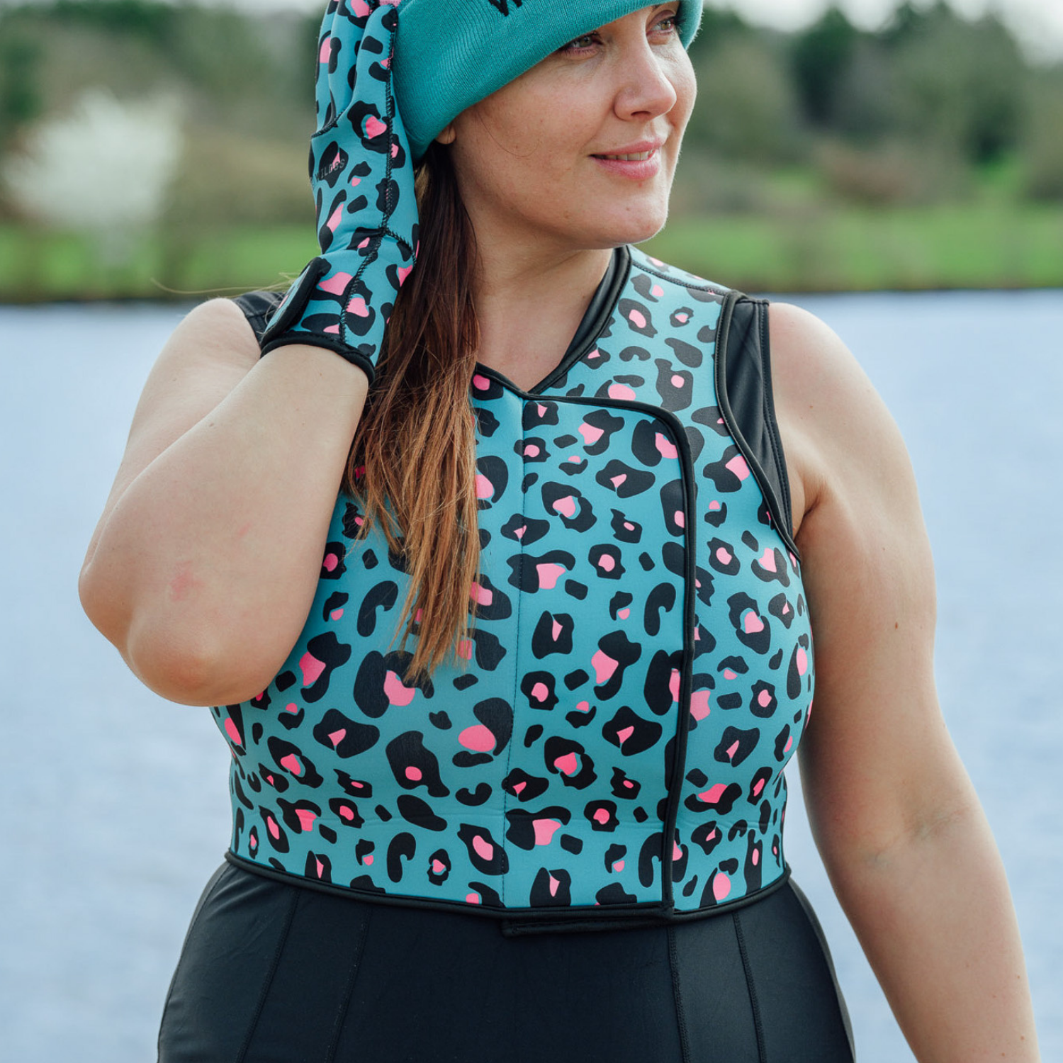 Woman wearing a teal neoprene body warmer pink and black leopard print pattern by a body of water.