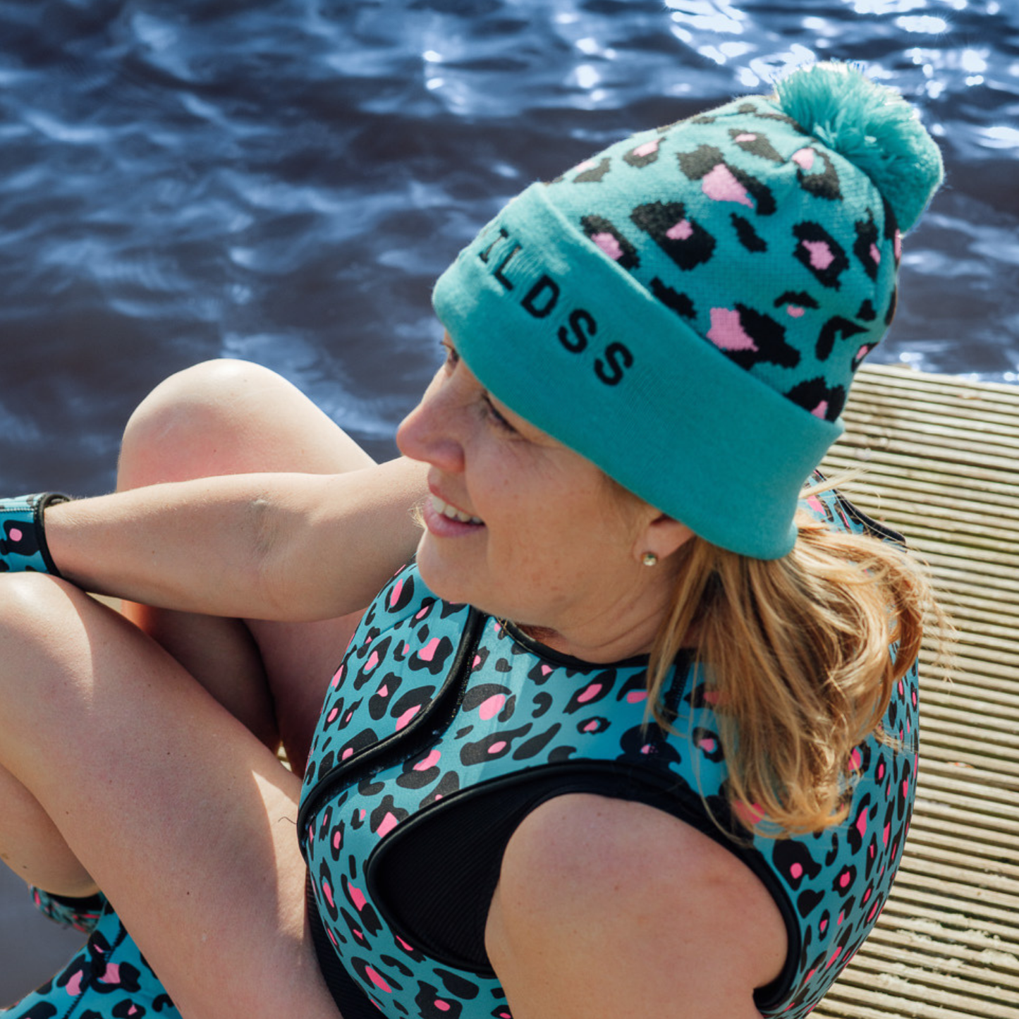 Person wearing a teal leopard print beanie and neoprene life jacket by water