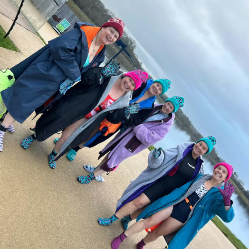 Group of people in colorful outfits and hats standing on a sidewalk.
