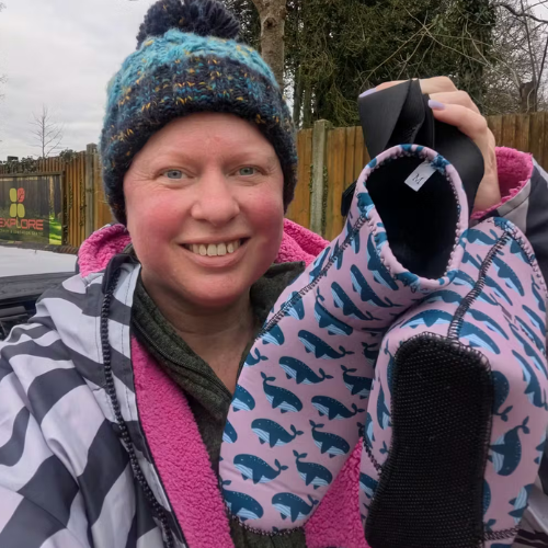 Person holding a pair of pink and blue patterned neoprene swimming shoes outdoors