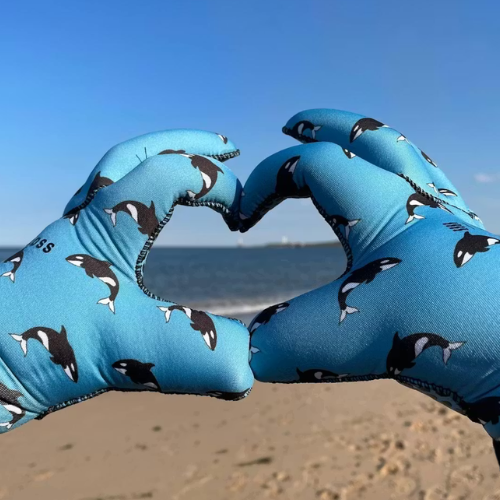 Blue neoprene swimming gloves with whale pattern forming a heart shape on a beach