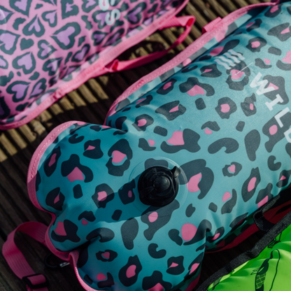 Two colorful leopard inflated tow floats with pink straps on a textured surface.