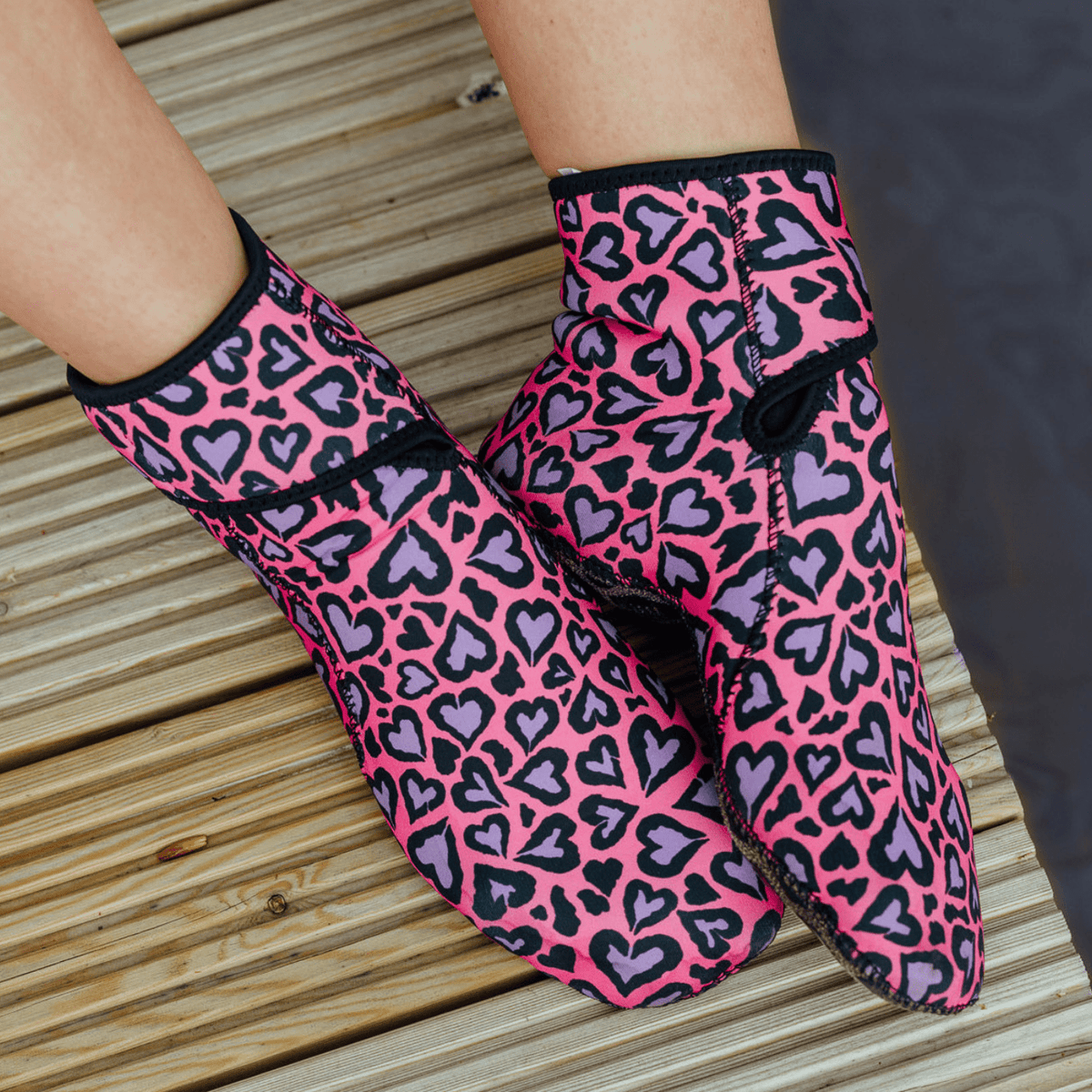 Pink and purple heart-patterned neoprene socks on a wooden surface