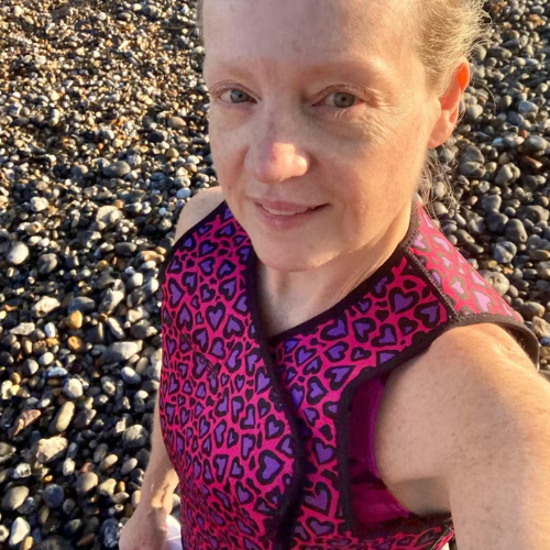 Person wearing a pink and purple neoprene body warmer on a pebbly beach