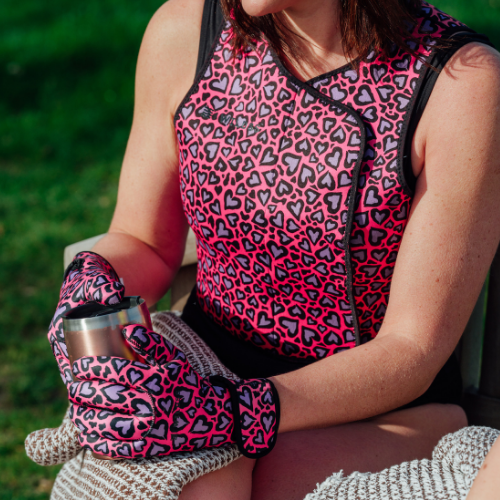 Person wearing a pink and black patterned body warmer and gloves, sitting outdoors.