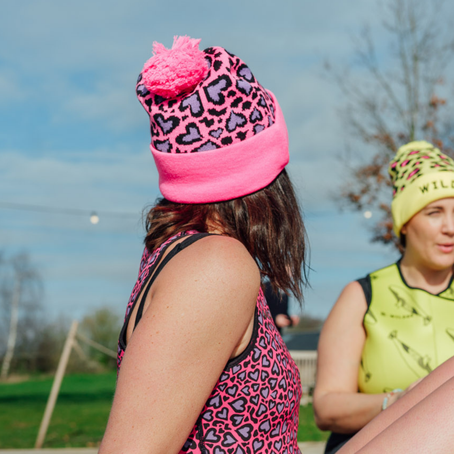 Two people wearing pink and leopard print hats outdoors with a clear sky.
