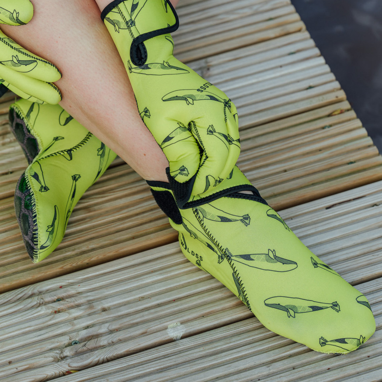 Yellow neoprene gloves with velcro strap and whale pattern on a wooden surface