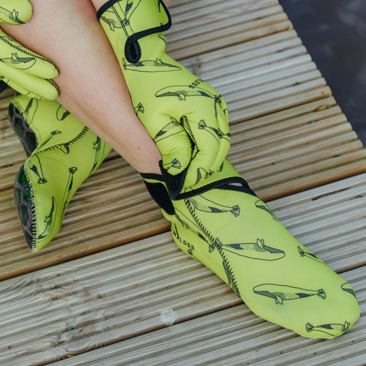 Yellow neoprene gloves with velcro strap and whale pattern on a wooden surface