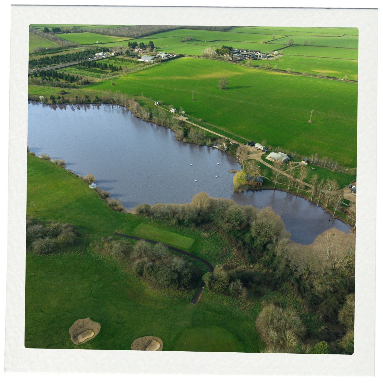 Aerial view of a lake surrounded by green fields and trees