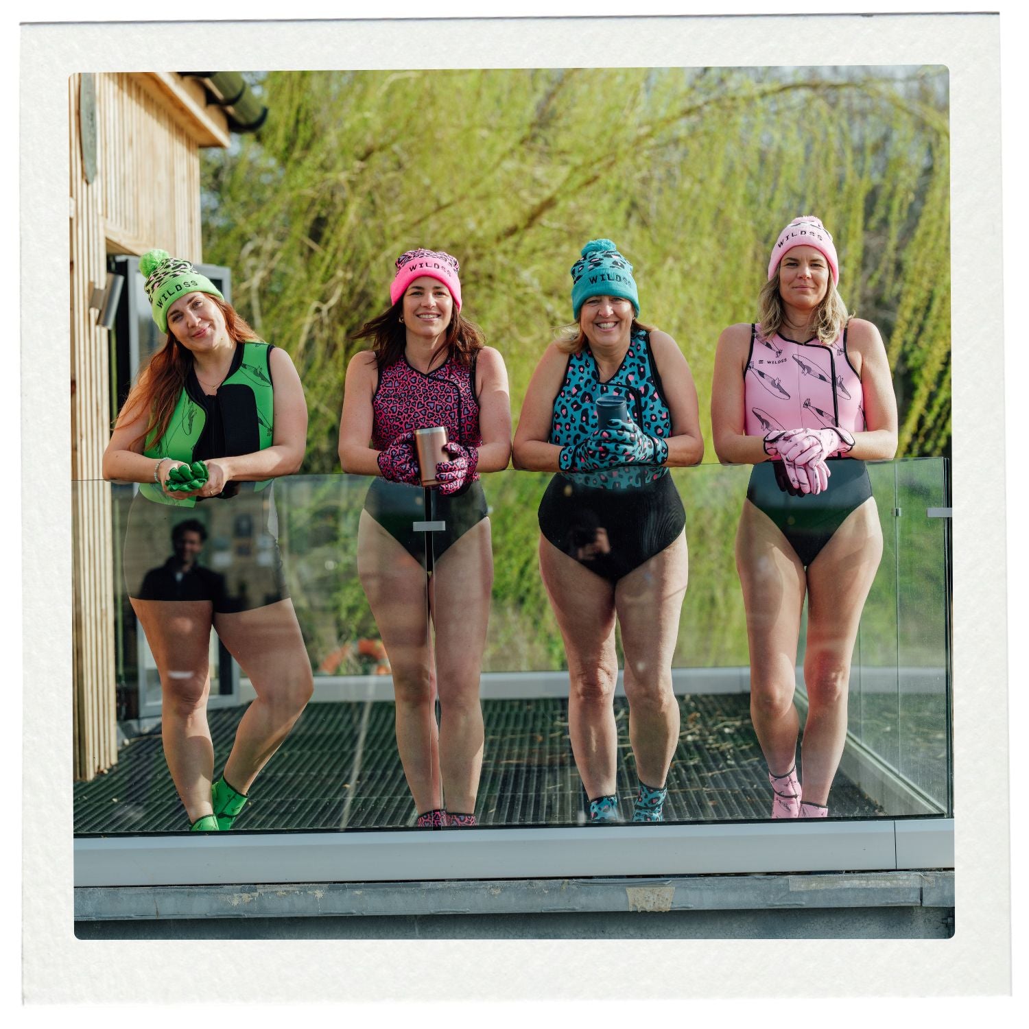 Four women in swimsuits and beanies standing on a glass platform outdoors.