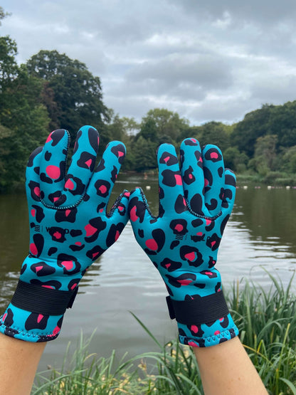 Close-up of turquoise leopard print neoprene swimming gloves with textured grip palms, hands raised by a lake