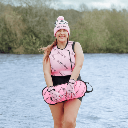 Person wearing pink hat, tow float and neoprene swimming gear by water.
