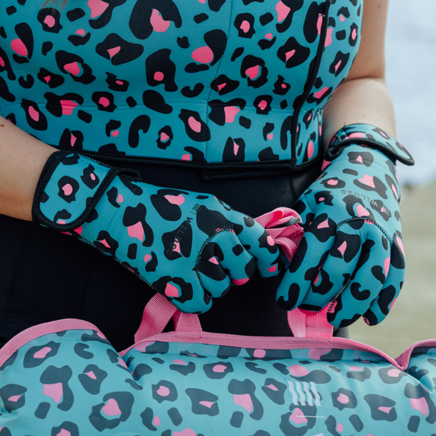 Person wearing turquoise neoprene gloves with black and pink leopard print and a matching neoprene body warmer and tow float