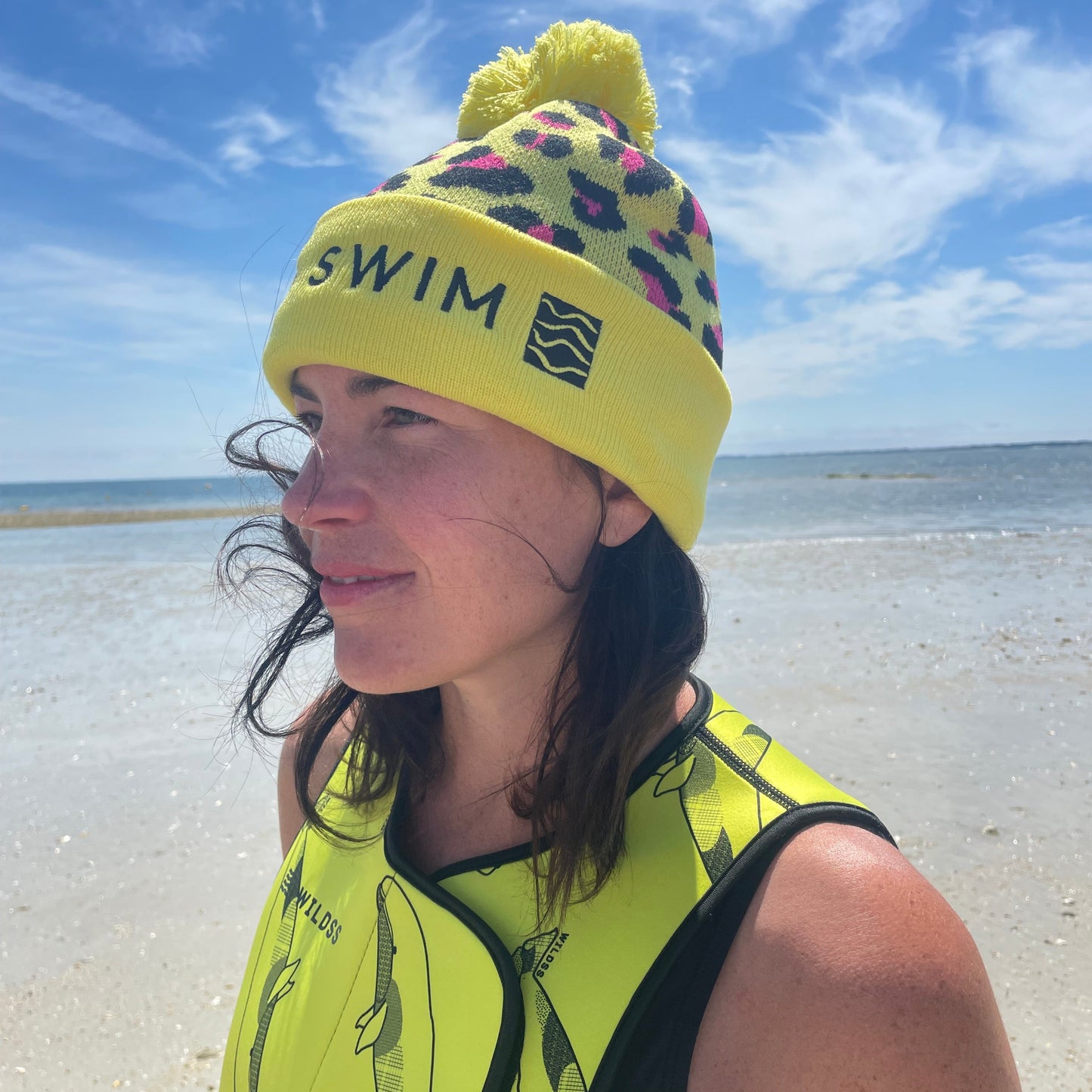Person wearing yellow leopard print hat and neoprene swimming gear by water.