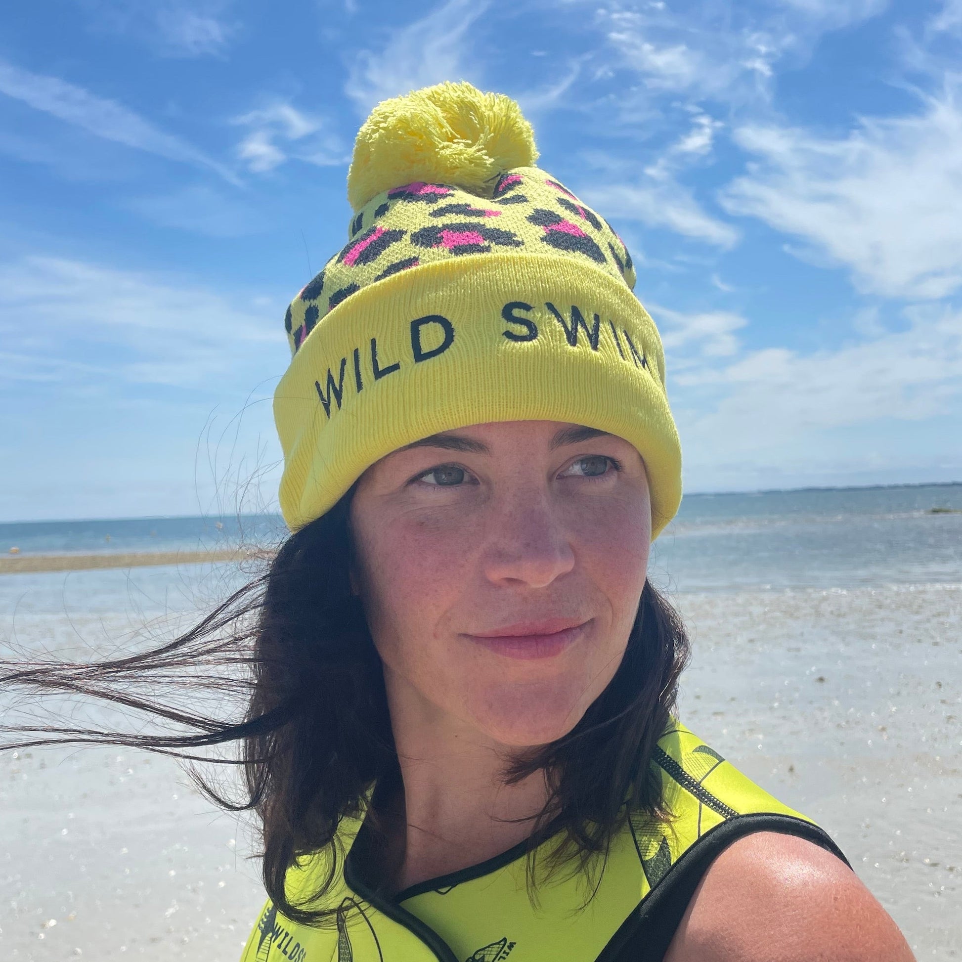 Person wearing yellow leopard print hat and neoprene swimming gear by water.