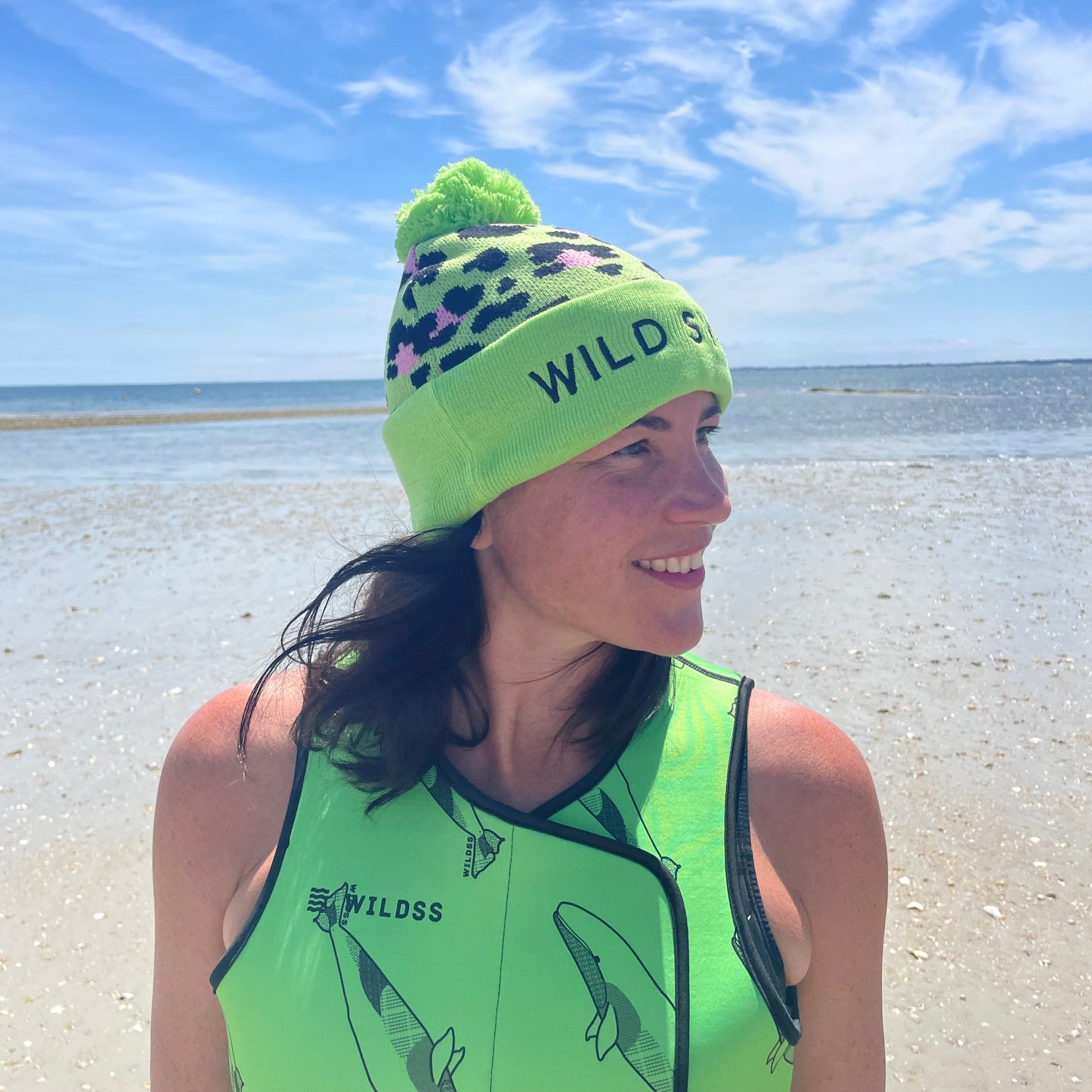 Person wearing green leopard print hat and neoprene swimming gear by water.