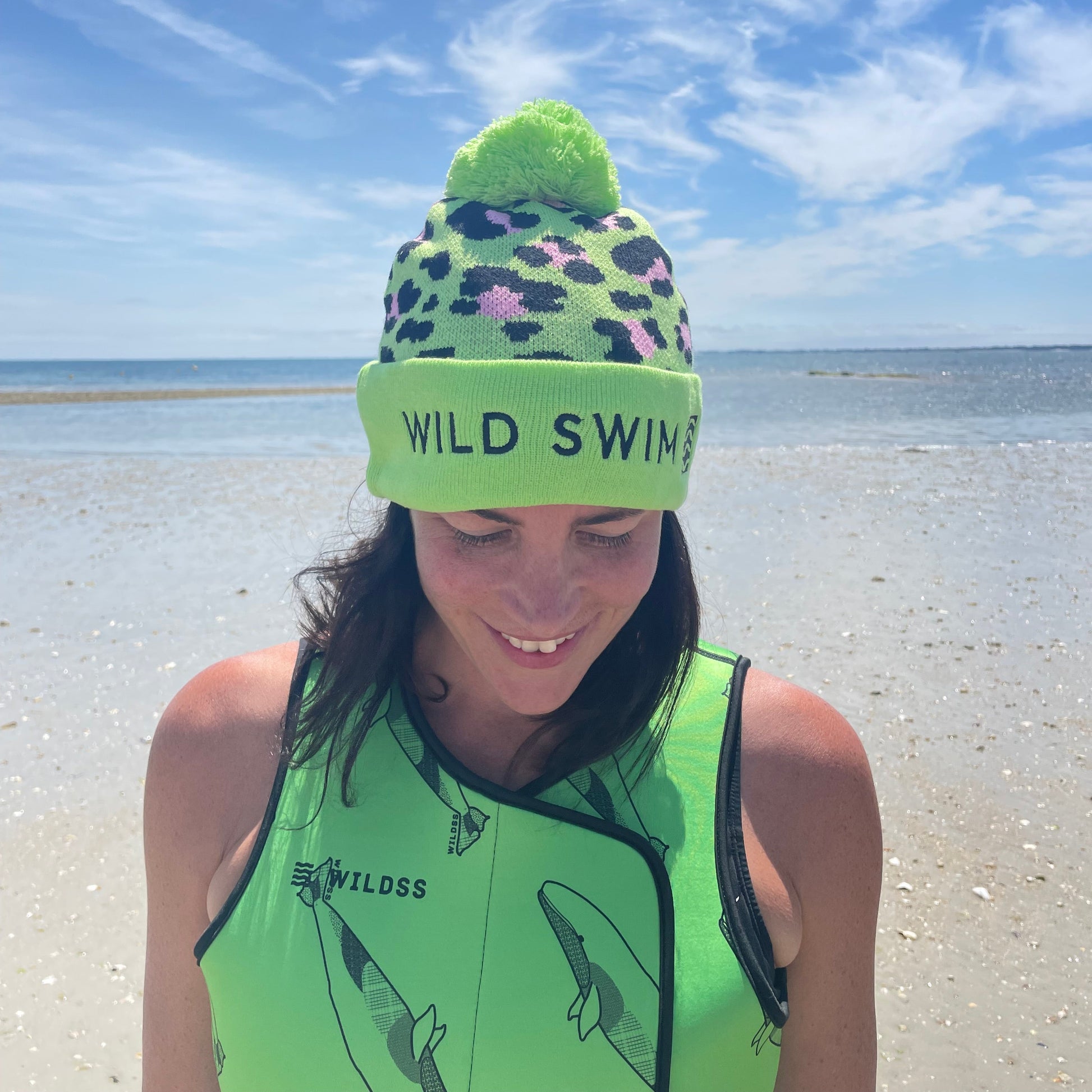 Person wearing green leopard print hat and neoprene swimming gear by water.