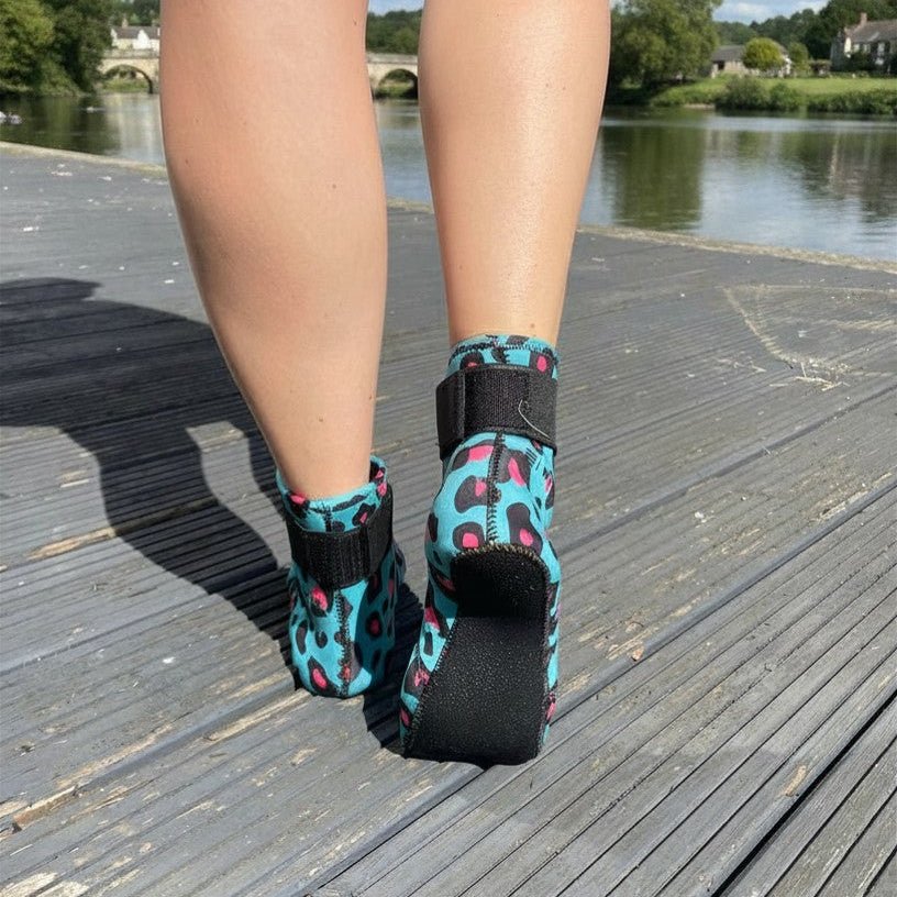 Back view of person wearing turquoise leopard print neoprene swimming socks on a wooden boardwalk