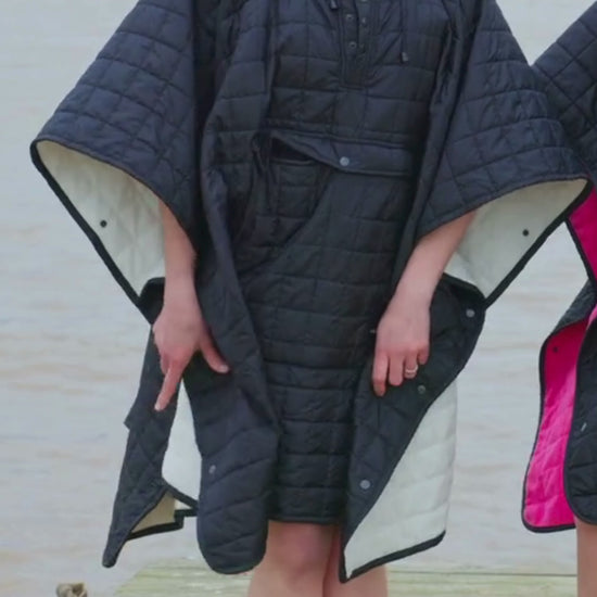 Video of woman wearing weatherproof black robe with large front pocket, side popper fastening, hood and fleece lining