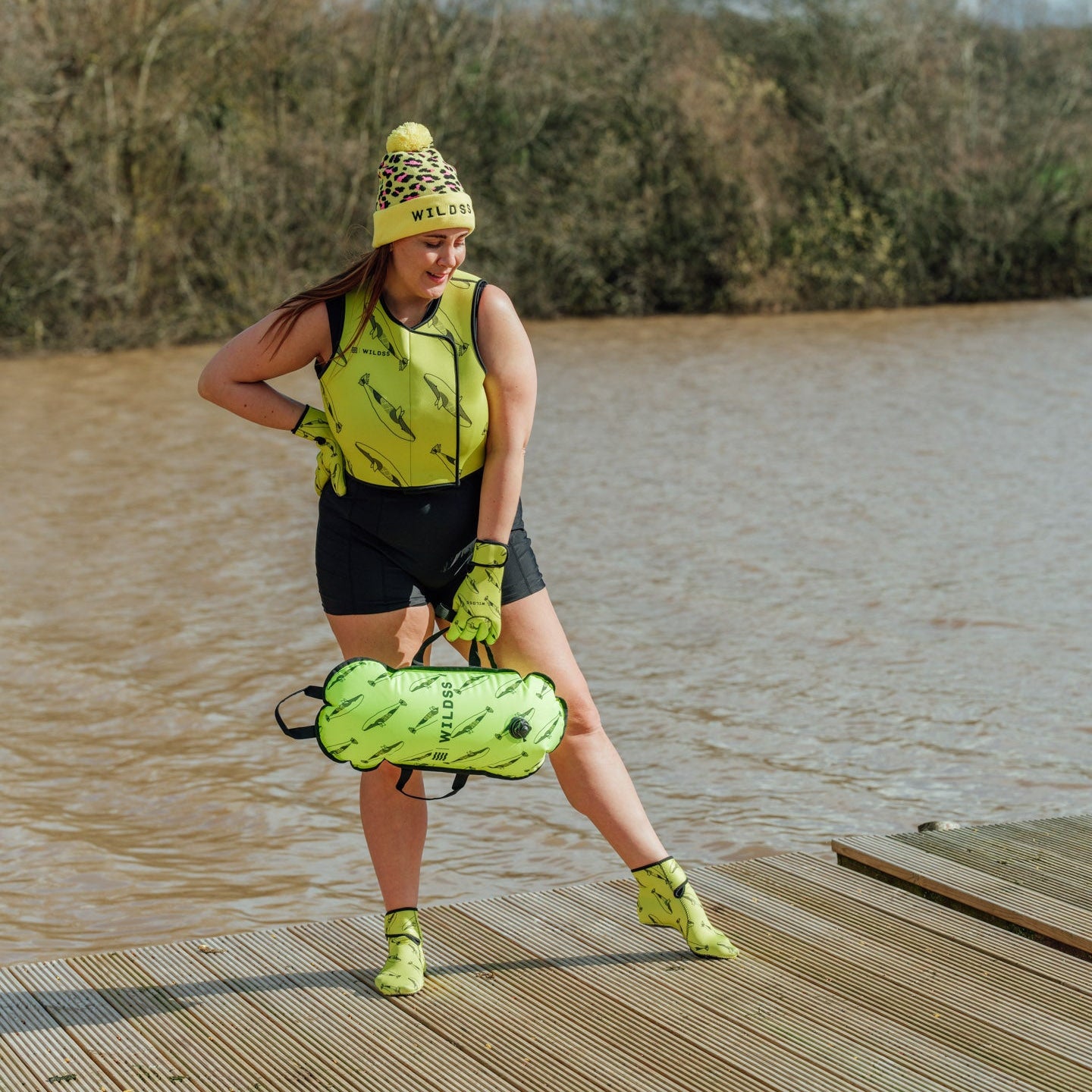 Person wearing yellow leopard print hat and neoprene swimming gear by water.