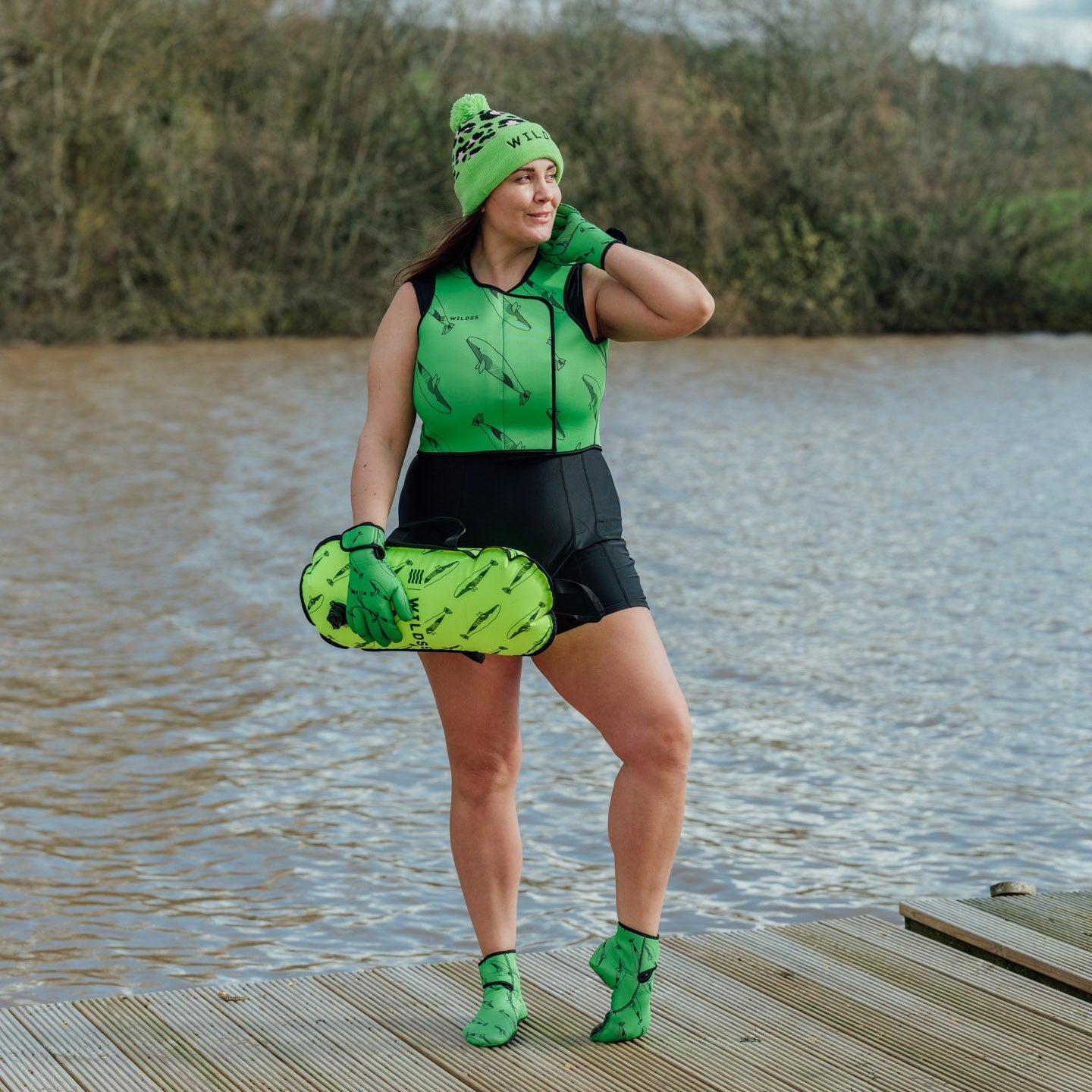 Person wearing green  leopard print hat and neoprene swimming gear by water.