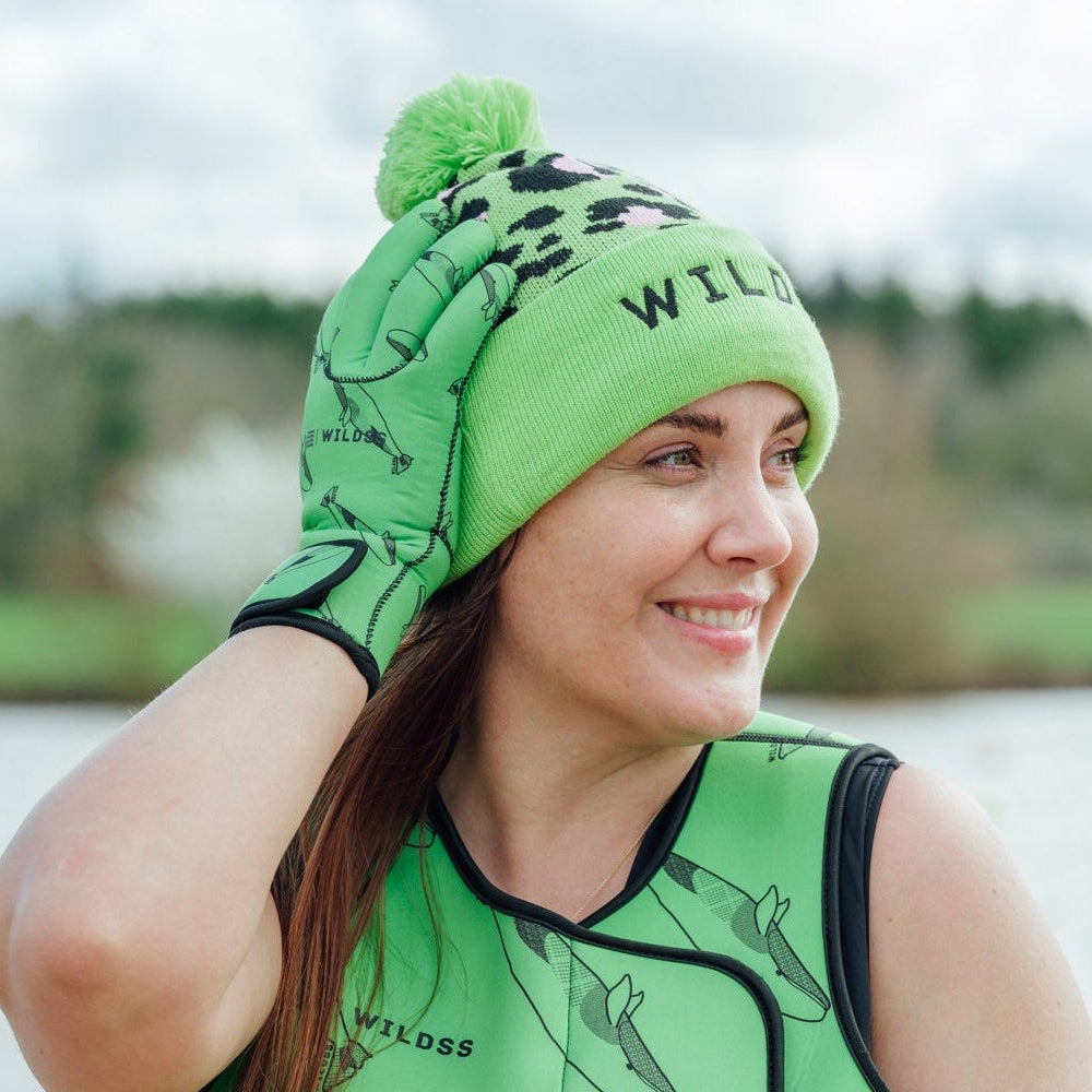 Person wearing green leopard print hat and neoprene swimming gear by water.